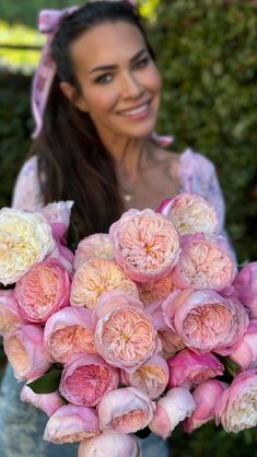 a woman holding a bouquet of pink and white flowers in front of her face smiling