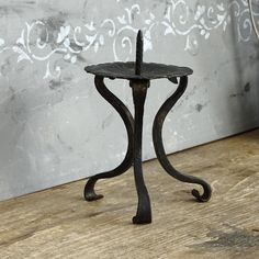 a small metal stand on top of a wooden floor next to a wall with an ornate design