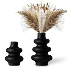 two black vases with dried grass in them on a white background, one is empty