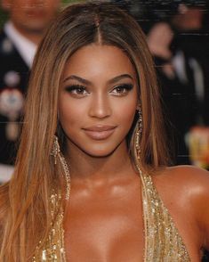 a close up of a woman with long hair wearing gold dress and large hoop earrings