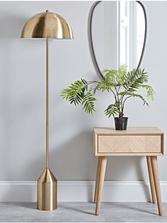 a gold lamp next to a table with a potted plant on it and a mirror in the background