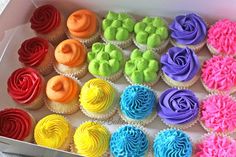 a box filled with lots of colorful cupcakes on top of a white table