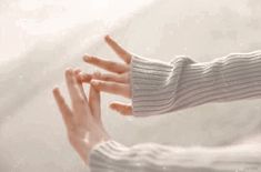 a woman's hand with her fingers extended out in front of the camera, while wearing a white sweater