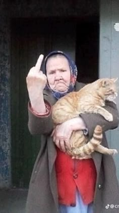 a man holding a cat in his arms and giving the peace sign with both hands