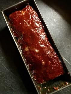 a metal pan filled with meat covered in marinara sauce on top of a table