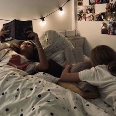 two women laying in bed reading books under string lights