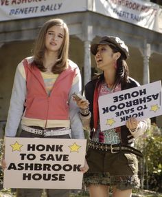 two young women holding signs in front of a house that says honk to save ash brook house