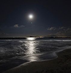 the moon is shining brightly over the water at night on the beach with waves coming in