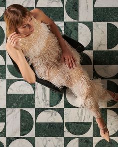 a woman laying on top of a black chair next to a wall covered in green and white tiles