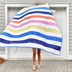 a woman holding up a colorful quilt in front of a garage door