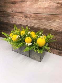 an arrangement of lemons and greenery in a wooden box on a white table