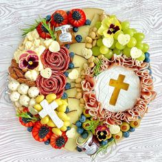 a cross made out of cheese, grapes, nuts and other food on a platter