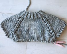 a gray knitted bag sitting on top of a wooden floor next to a pair of pink scissors