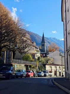 cars parked on the side of a road in front of buildings and a church steeple