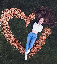 a woman laying on the ground with leaves in her heart shaped frame, looking up at the camera