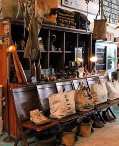 several purses are lined up on a bench in a shop with many bags hanging from the wall