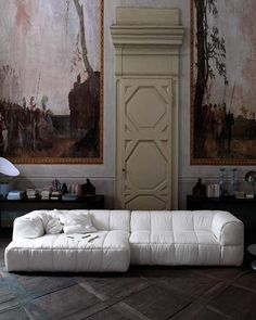 a white leather couch sitting in front of a painting on the wall next to a lamp