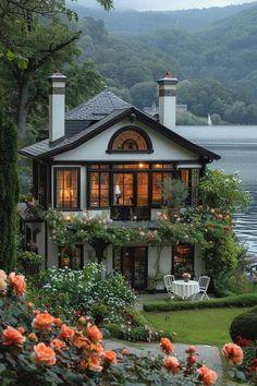 the house is surrounded by beautiful flowers and greenery, with a lake in the background