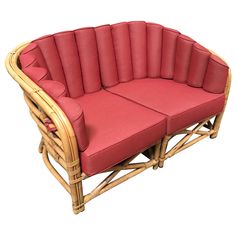 a wicker couch with red cushions on it's back and arms, sitting in front of a white background