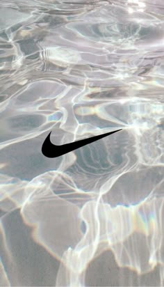 a black nike logo is floating in the clear blue water with sunlight reflecting on it