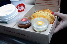 a person holding a box with some food in it and two cups on the side