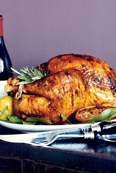 a roasted turkey on a plate with garnishes and wine bottle in the background