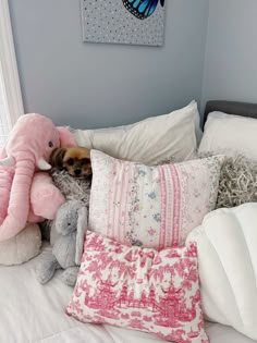 a small dog laying on top of a bed next to pillows and stuffed animal toys