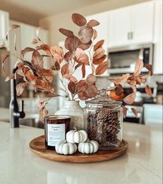 an arrangement of candles, leaves and pumpkins on a tray in a kitchen setting