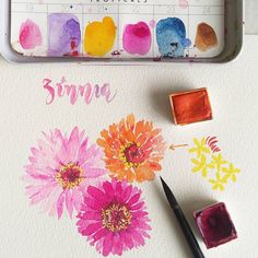 some watercolors are sitting on a table next to a paint tray with flowers