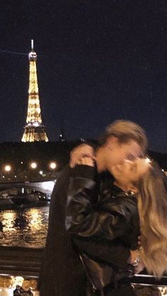 a man and woman kissing in front of the eiffel tower, at night