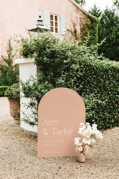 a sign that is on the ground near some flowers and bushes in front of a building