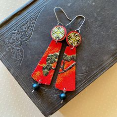 two pairs of red and yellow earrings on top of a black book with blue beads