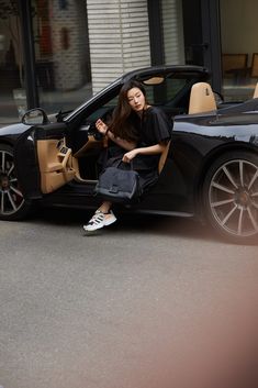 a woman sitting in the open door of a black sports car with her handbag