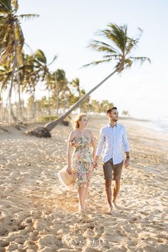 a man and woman walking on the beach holding hands with palm trees in the background