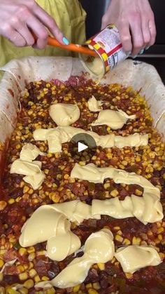 a person pouring sauce onto a dish with corn on the cob and other toppings