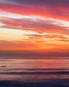 the sun is setting over the ocean with surfers out in the water on their surfboards