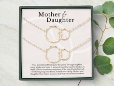 the mother and daughter necklaces are on display in a box with greenery next to it