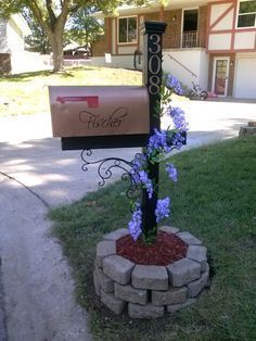 a mailbox with flowers in the middle of it next to a brick planter