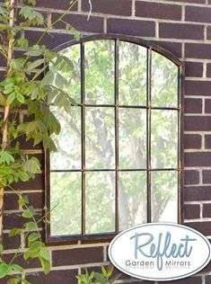 a mirror hanging on the side of a brick wall next to a window with vines growing out of it