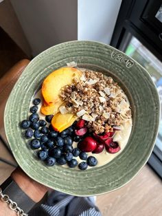 a bowl of oatmeal with fruit and granola on top, in front of a window