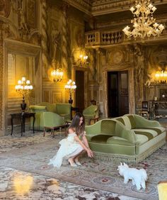 a woman kneeling down next to a green couch in a room with chandeliers