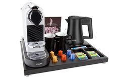 a coffee maker, cups and other items on a black tray with white background for display