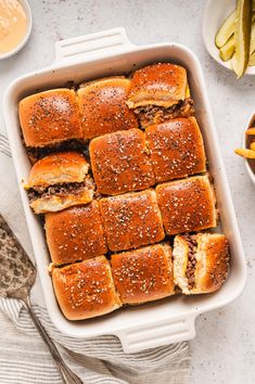 a white casserole dish filled with sliders and french fries next to dipping sauce