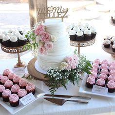 a table topped with lots of cupcakes covered in white frosting and pink flowers