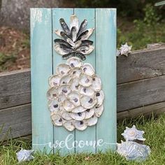 a wooden sign with seashells on it sitting in the grass next to a fence