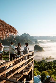 three people sitting at a table on top of a hill overlooking the foggy valley