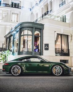 a green sports car is parked in front of a white building with windows and balconies