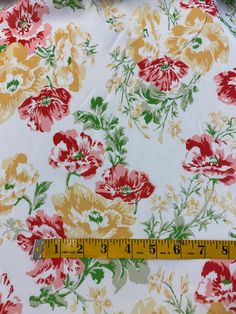 a ruler is measuring the width of a flowered print fabric with red, yellow and green flowers on it