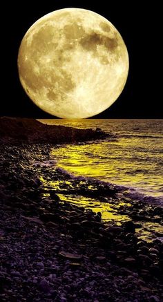 the full moon is shining brightly over the water and rocks on the beach at night