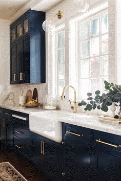 a kitchen with dark blue cabinets and white counter tops, gold pulls on the faucet